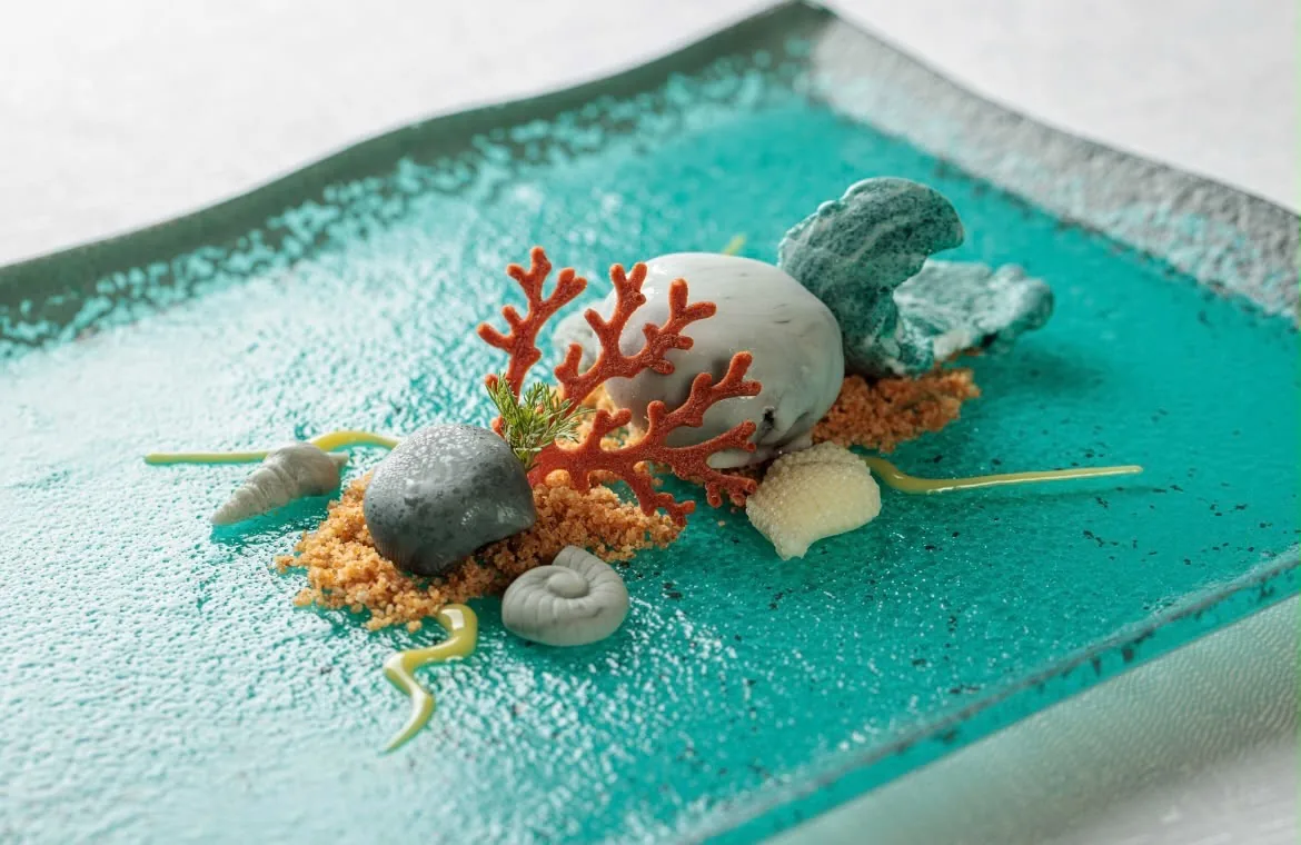 Dessert ispirato al mare con decorazione a corallo rosso e sfere su piatto turchese