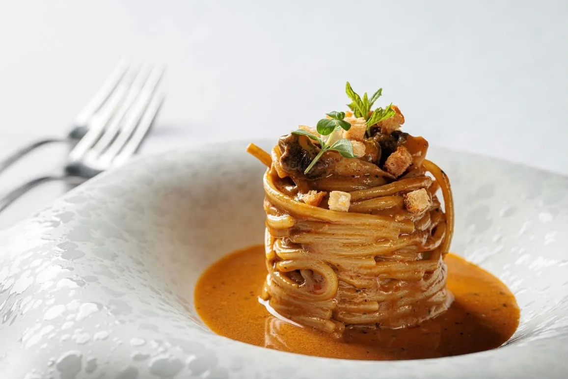 Nido di spaghetti con salsa rossa sormontato da crostini dorati ed erbe aromatiche in un piatto fondo bianco