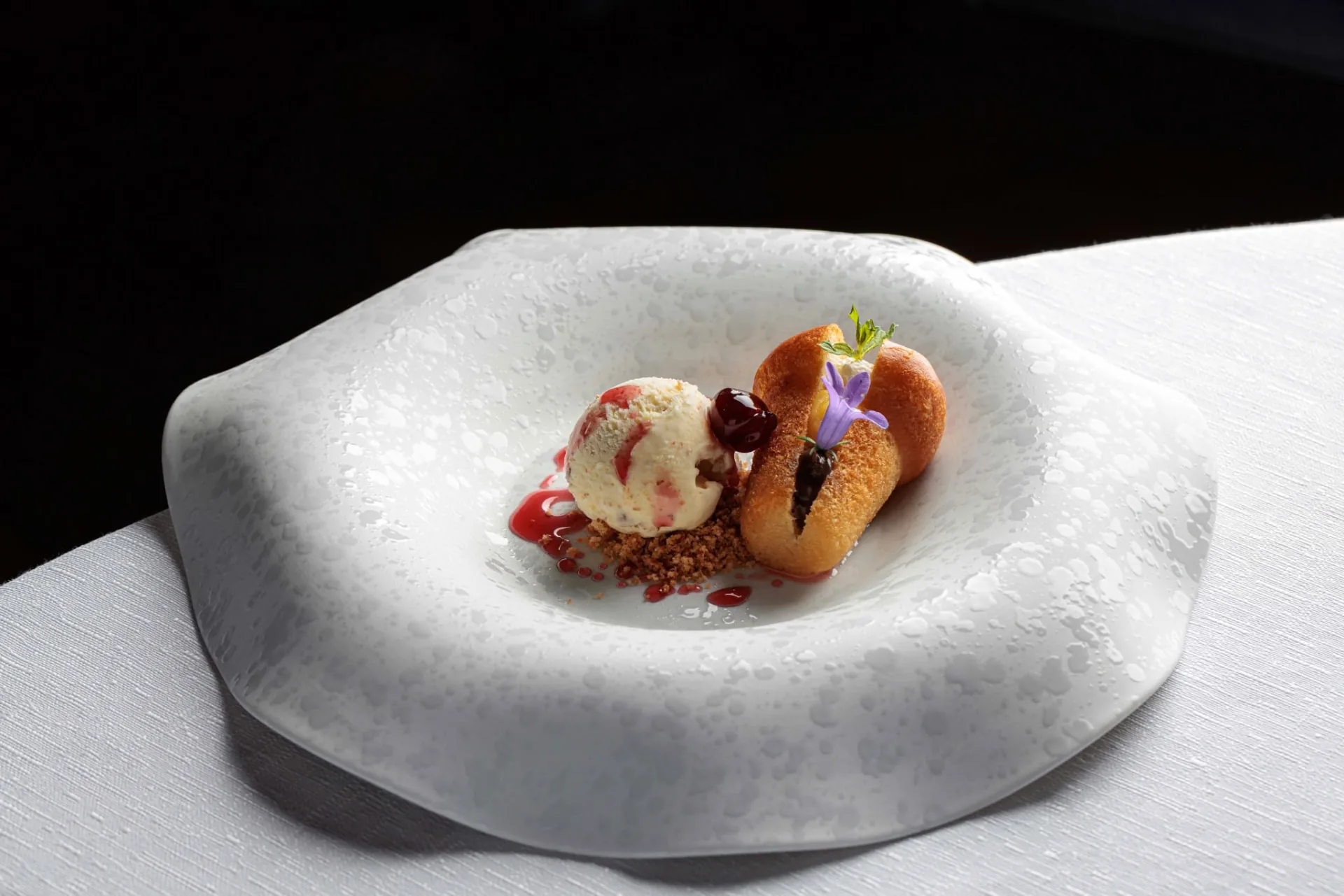 Composizione gastronomica con crema chiara, elementi dorati e fiori eduli su piatto bianco sagomato