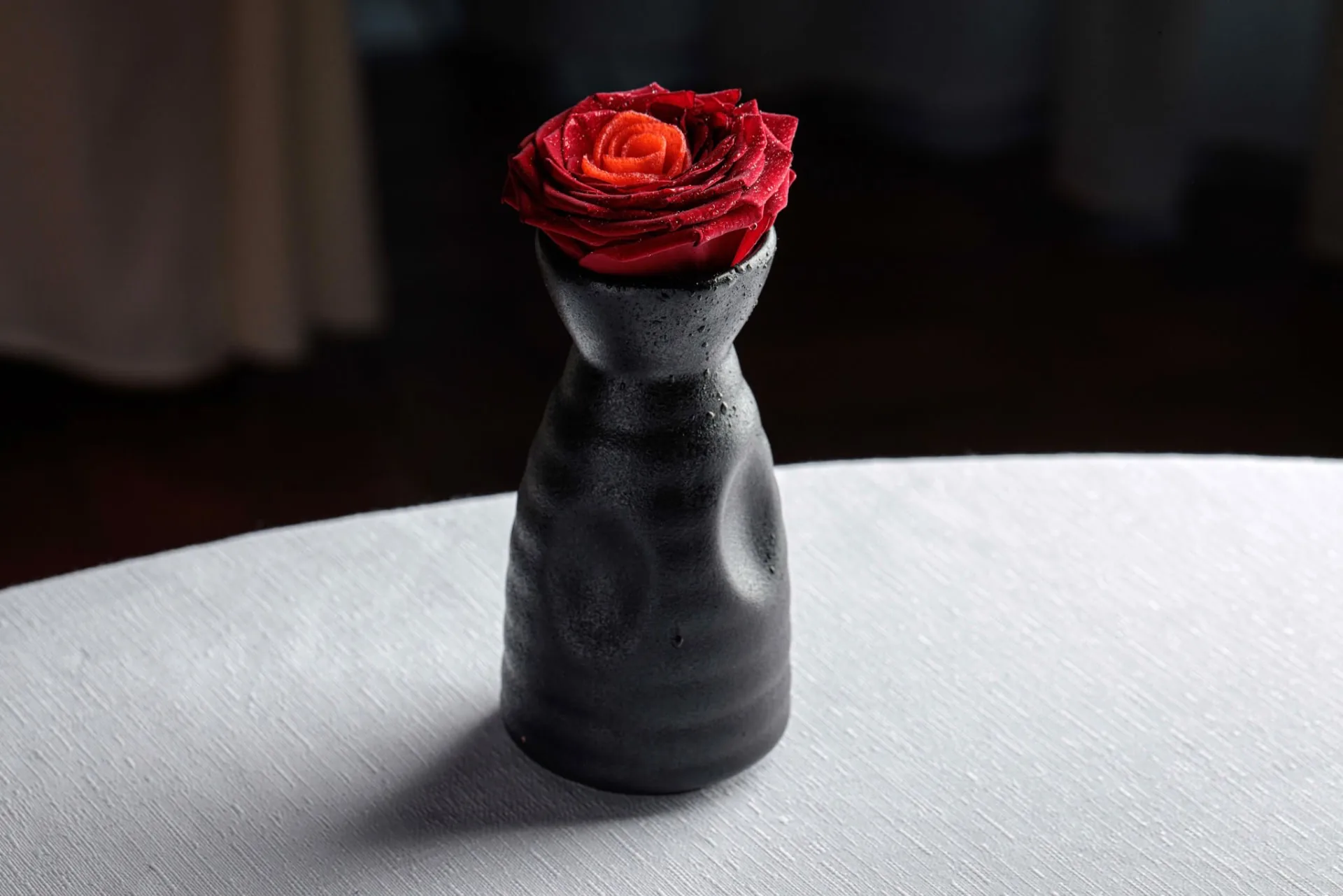 Rosa rossa in un piccolo vaso nero su una tavola con tovaglia bianca