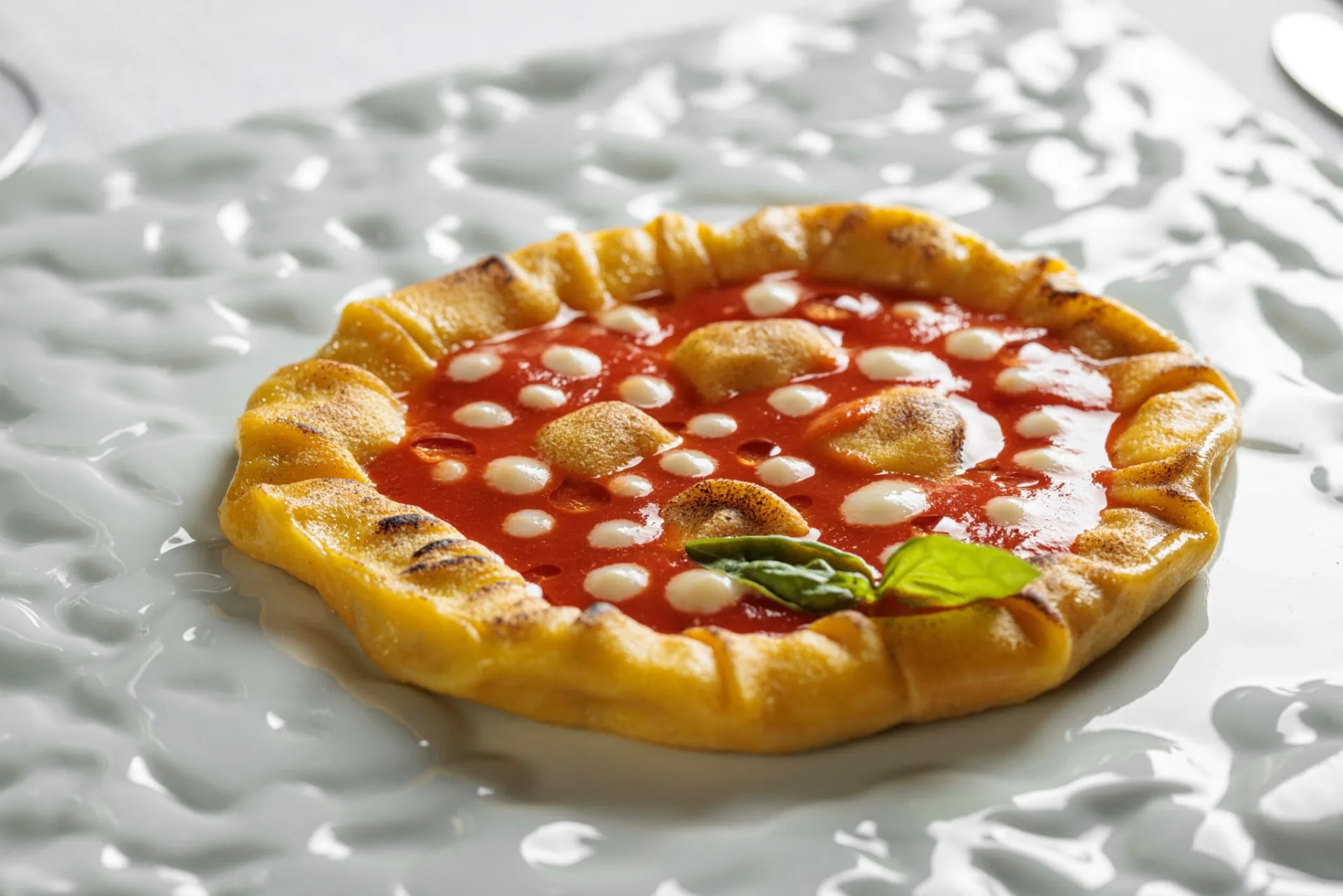 Tartelletta dorata con salsa rossa, piccoli punti di crema bianca e foglie verdi