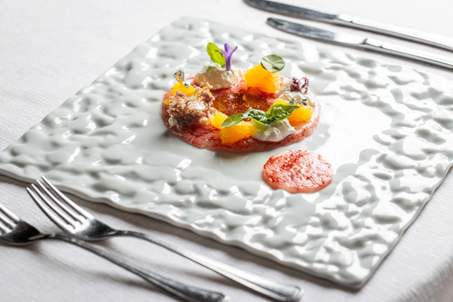 Composizione gastronomica con verdure colorate, fiori eduli e salsa rosa su piatto bianco a rilievo