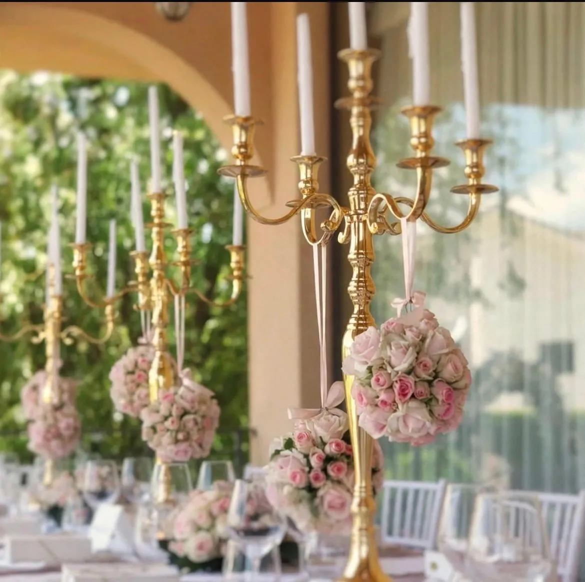 Candelabri dorati sormontati da sfere di rose per un allestimento di cerimonia