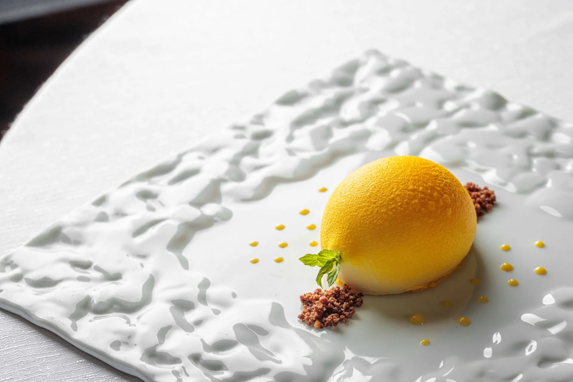 Dessert giallo a forma di limone con piccole guarnizioni su piatto bianco a rilievo