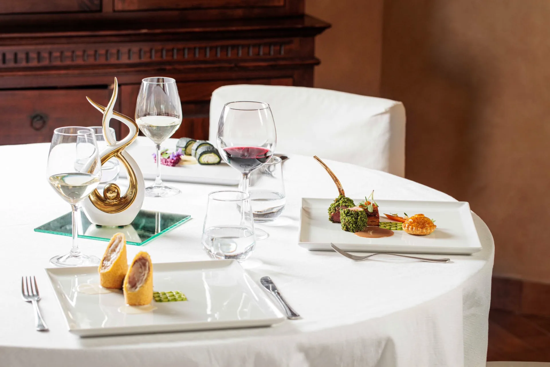 Tavola del ristorante con tovaglia bianca, calici, posate e piatti gourmet serviti